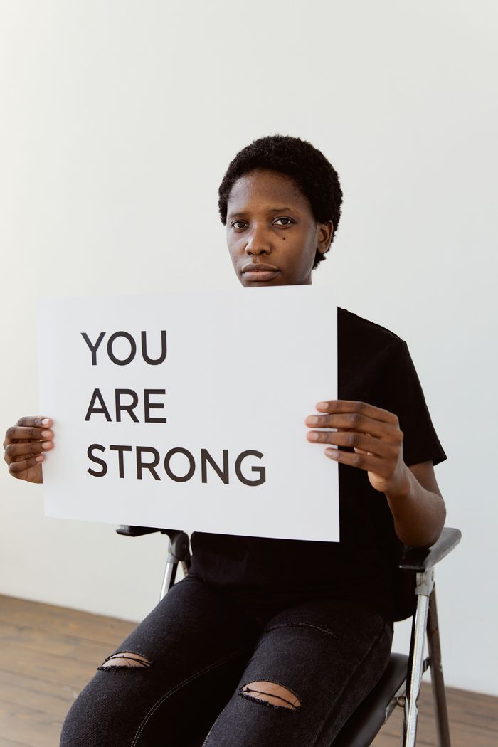 A portrait of a woman in a wheelchair holding a sign that reads 'YOU ARE STRONG,' promoting empowerment and resilience.